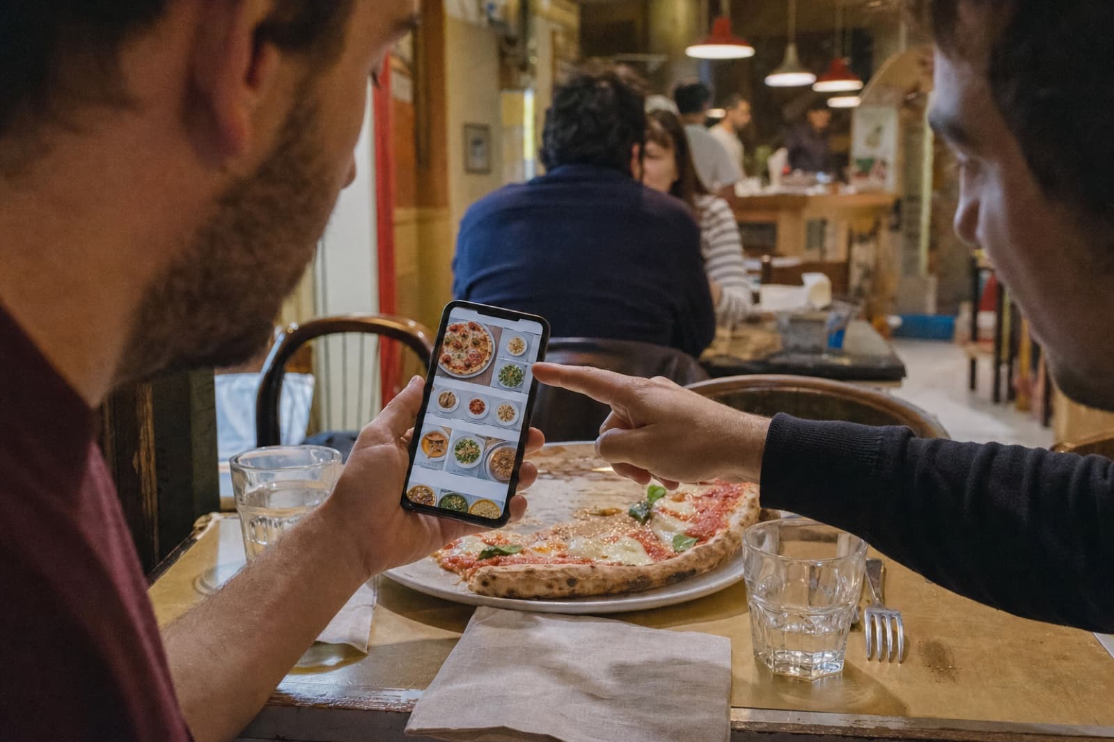 Due clienti consultano il menu digitale sul telefono in una pizzeria informale